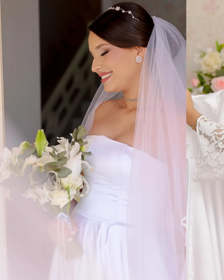 Noiva sorrindo de olhos fechados, com véu e buquê de lírios