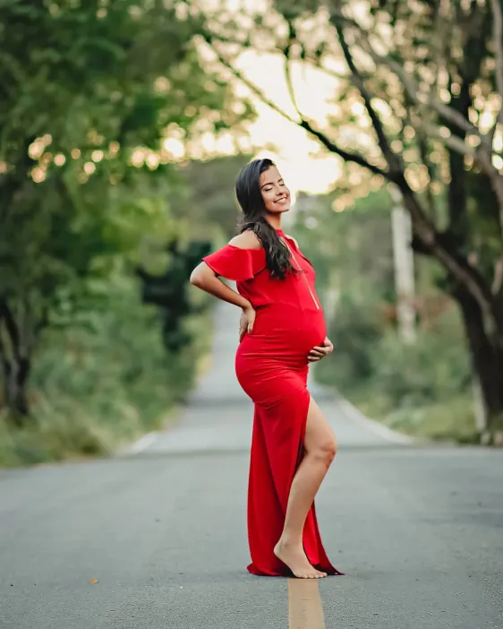 Gestante de vestido vermelho em uma estrada arborizada