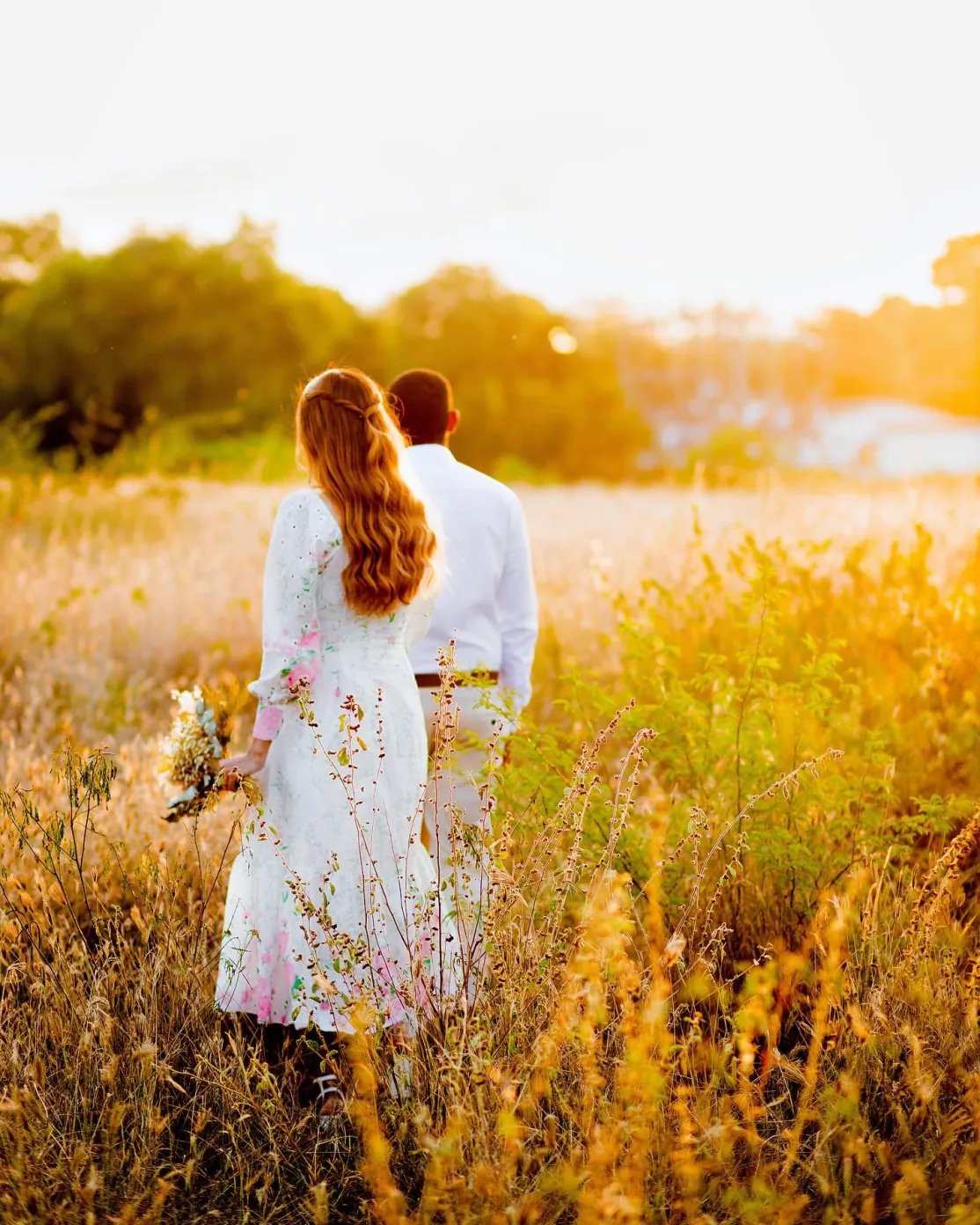 Casal caminhando em campo dourado ao entardecer